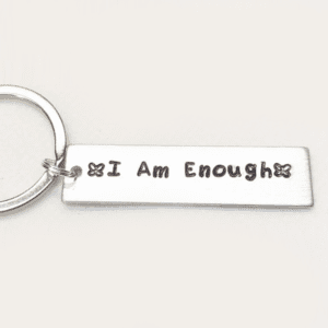 A silver key chain with the words " i am enough ".