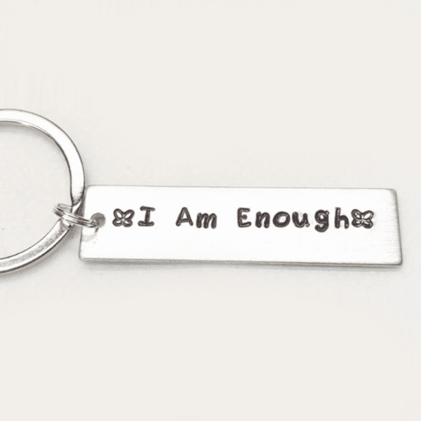 A silver key chain with the words " i am enough ".