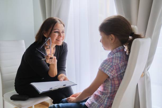 A woman talking to a girl in front of a window.