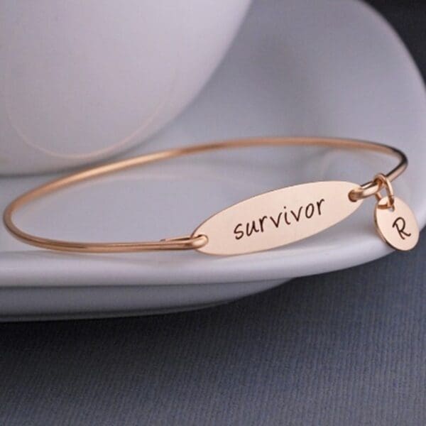 A gold bracelet with the word survivor on it.