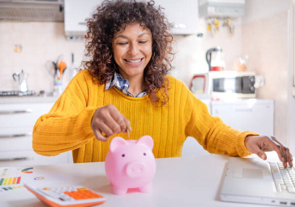 A woman putting money into a pink piggy bank.