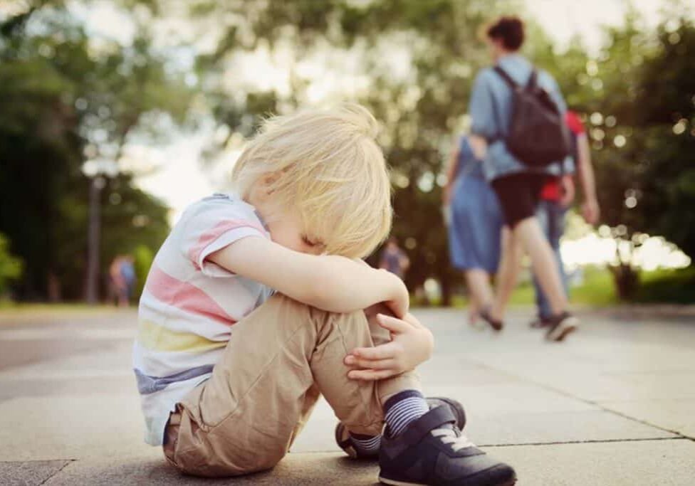 A young child sitting on the ground with his head down.