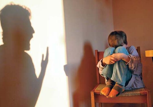 A child sitting on the back of his father.