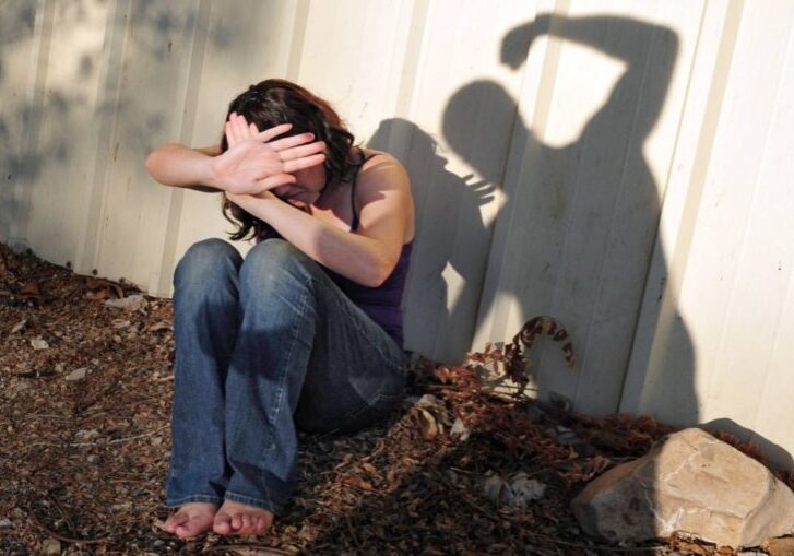 A woman sitting on the ground with her hands covering her face.