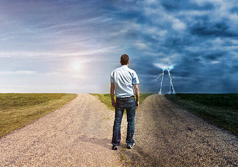 A man standing on the side of a road looking at two different roads.